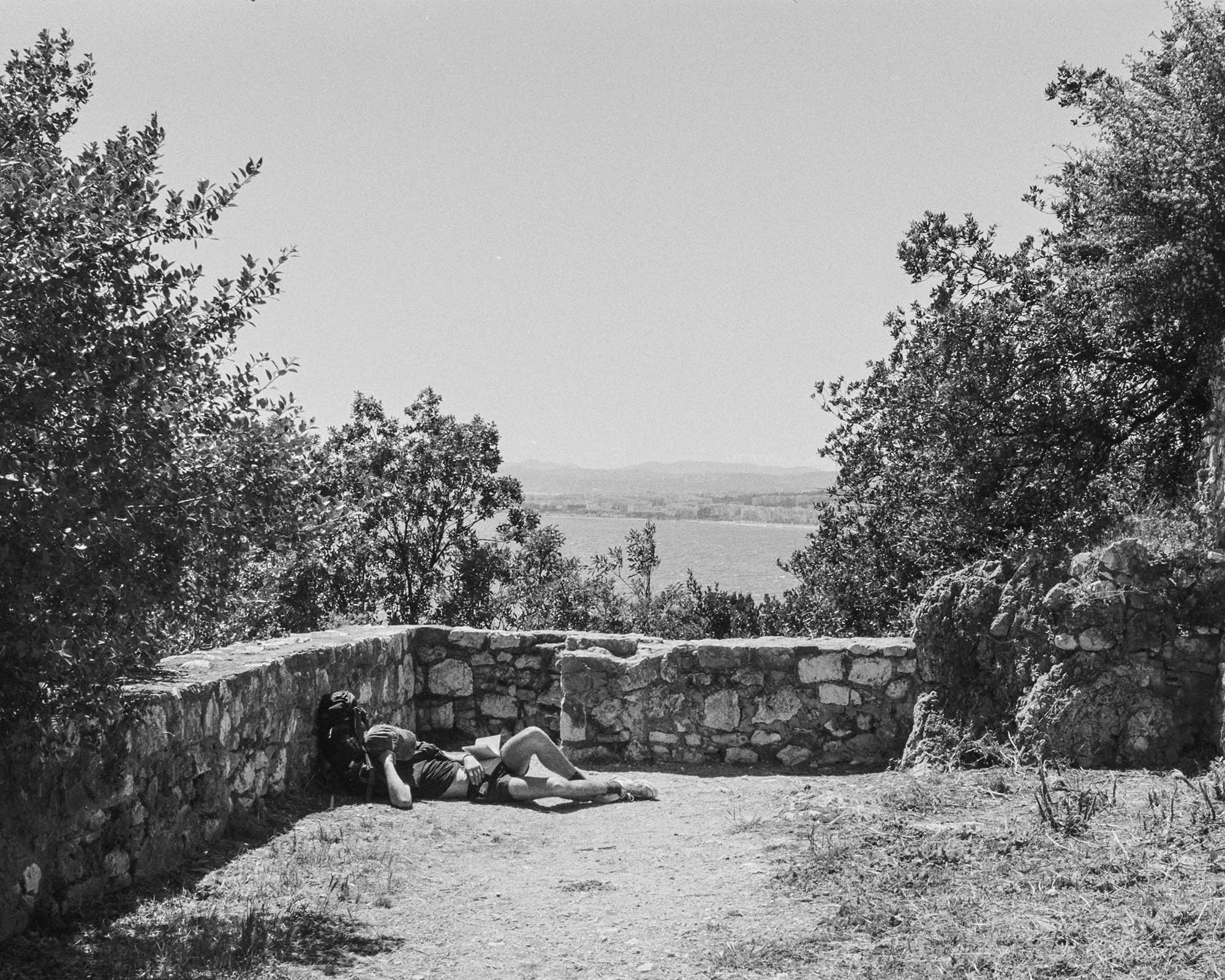 A man laying asleep in the sun with a open book on his lap.